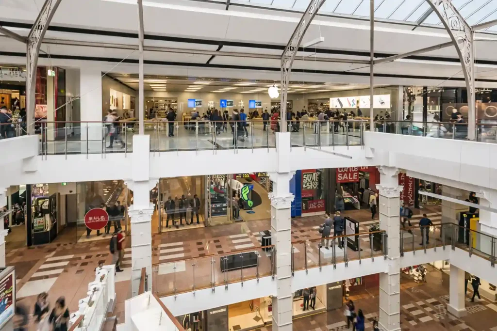 نمای داخلی مرکز خرید Broadway Sydney با چندین طبقه، فروشگاه Apple در طبقه بالا، راهروهای باز و حضور خریداران.