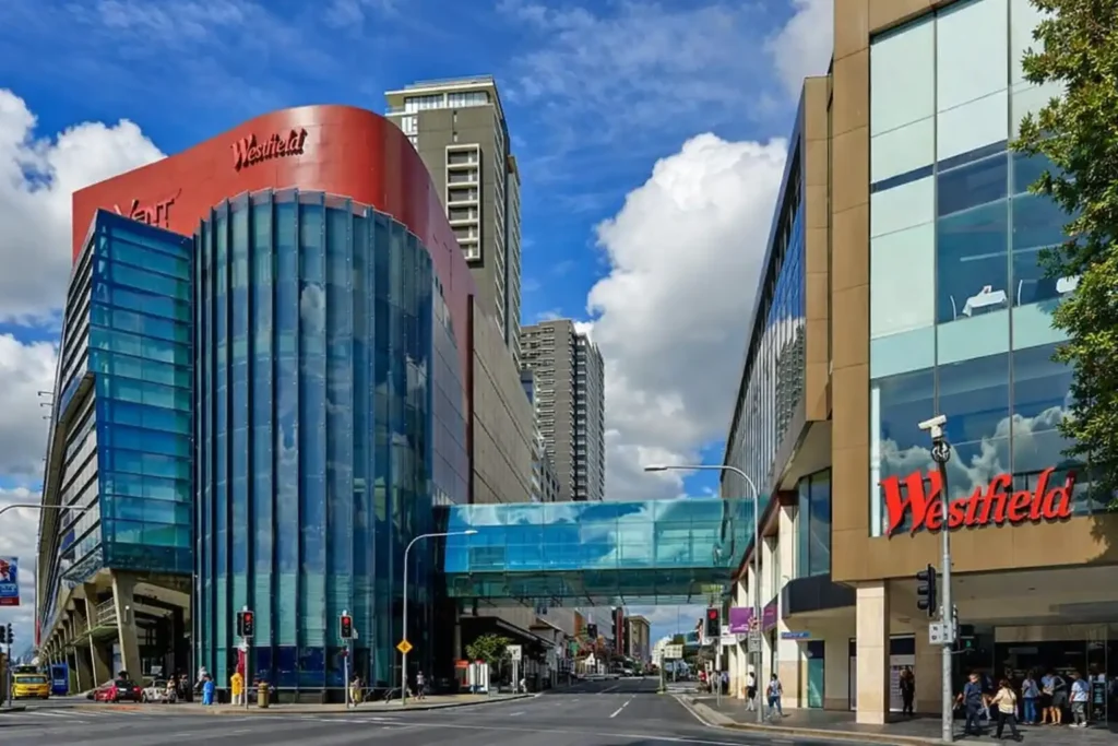 نمای بیرونی مرکز خرید Westfield Parramatta با ساختمان مدرن شیشه‌ای، پل هوایی شفاف بین دو بخش مرکز، خیابان شهری و لوگوی قرمز Westfield